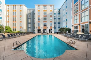 A swimming pool with lounge chairs and a building with multiple floors and balconies.
