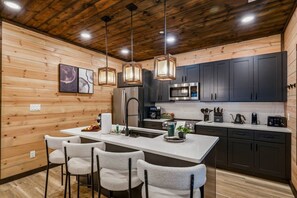 A modern kitchen with wooden walls, a central island, bar stools, and contemporary appliances. - 2 Rooftop Cabins Sleep 34 - Golf Sim - 2 Indoor Pools - 2 Game Rooms - 2Hot Tubs (Pigeon Forge)