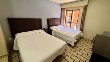 A hotel room with two beds, a small table, and a window with curtains.