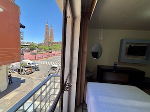 A hotel room with a bed, a TV, and a view of a street with a church and vehicles.