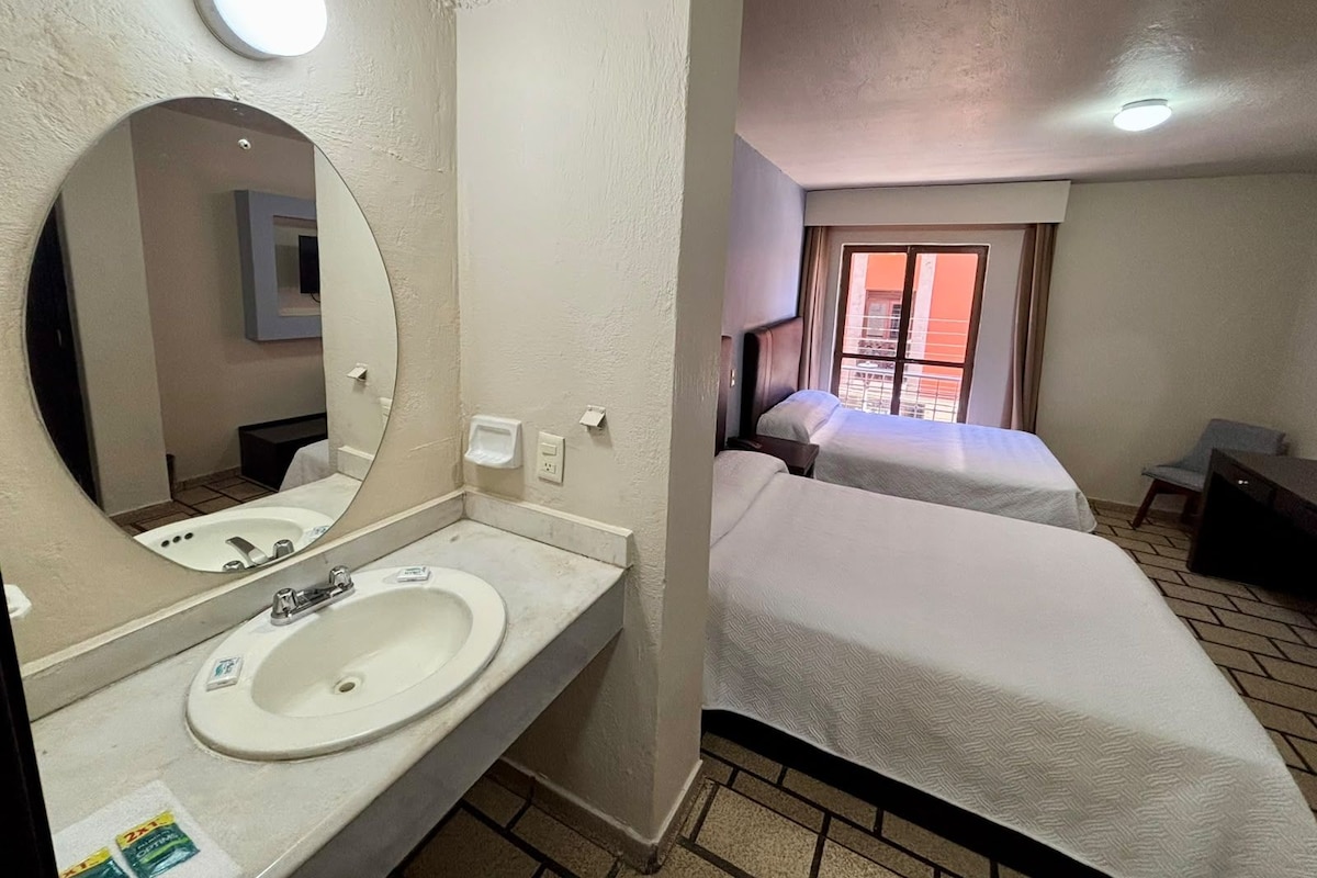 Une chambre d’hôtel avec salle de bain, un lit, un bureau et une fenêtre donnant sur un paysage agréable.