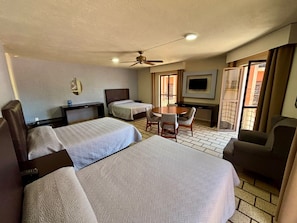 A hotel room with two beds, a dining table, a TV, and a ceiling fan.