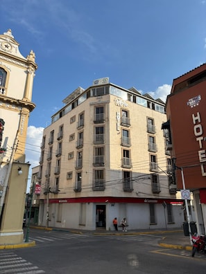 A multi-story hotel with balconies, a bar and restaurant on the ground floor, and a clock tower in the background.