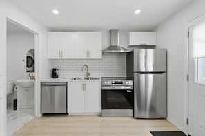 A compact kitchen with white cabinetry, a stainless steel refrigerator, a built-in oven, and a dishwasher. - Rodman Oasis 1BR, 1B with washer/dryer 28+ nights (St. Catharines)