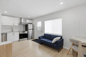 A modern kitchen with stainless steel appliances, a blue sofa, and a large window. - Rodman Oasis 1BR, 1B with washer/dryer 28+ nights (St. Catharines)