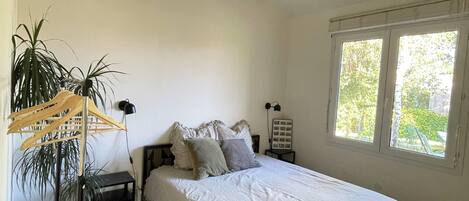 A bedroom with a bed, a hanging plant, a bedside table, a lamp, and a window.