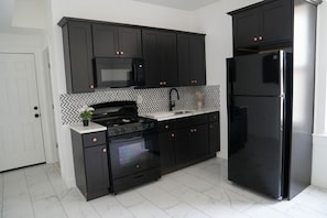 A kitchen with black cabinets, a microwave, a stove, an oven, and a refrigerator. - 2-bedroom apartment Minutes from NYC (Irvington)