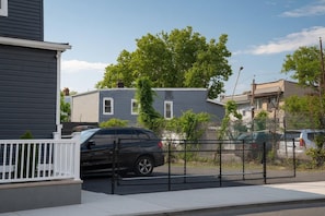 A residential area with a gated driveway, a parked SUV, and houses with visible windows and a tree. - 2-bedroom apartment Minutes from NYC (Irvington)