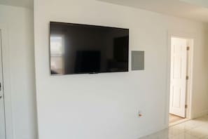 A room with a flat-screen TV mounted on the wall, a door, and a light switch. - 2-bedroom apartment Minutes from NYC (Irvington)