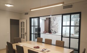 A modern dining area with a large table and chairs, a kitchen visible through a glass partition, and a door leading to another room. - Spacious Downtown Apartment with a Jacuzzi (Córdoba)