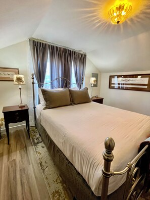 A bedroom with a bed, two bedside tables, a nightstand, a wall-mounted lamp, a ceiling light fixture, and a framed picture on the wall.