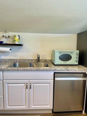 A kitchen with a stainless steel sink, a microwave, and white cabinetry.