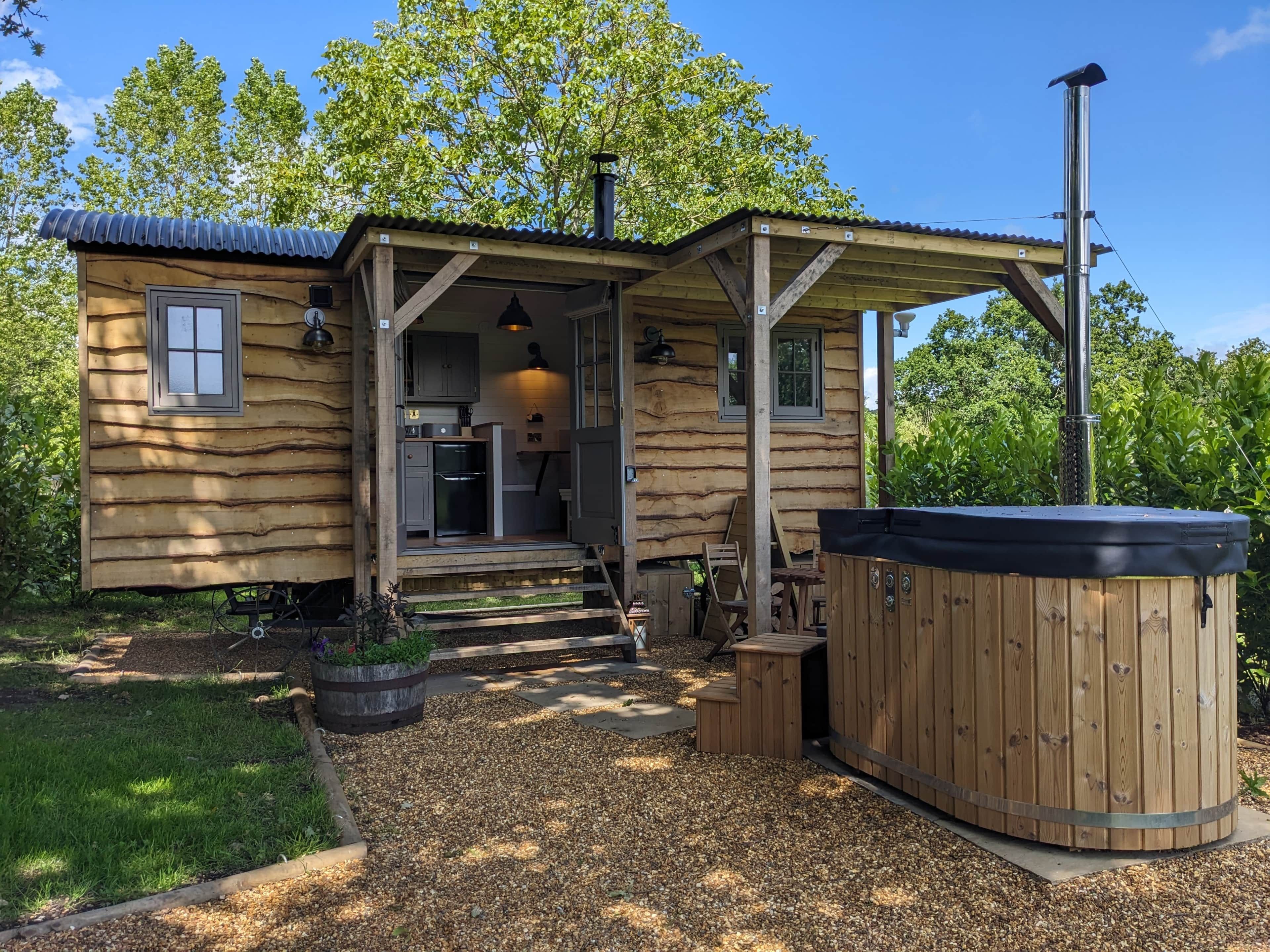 Une cabane en bois dotée d’un porche couvert, d’un jacuzzi et d’une petite cuisine extérieure.