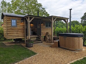A wooden cabin with a porch, a hot tub, and a small outdoor seating area.