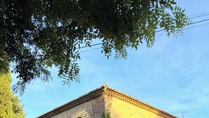 Edifício de pedra com telhado de cerâmica, cercado por vegetação densa e um caminho de cascalho.