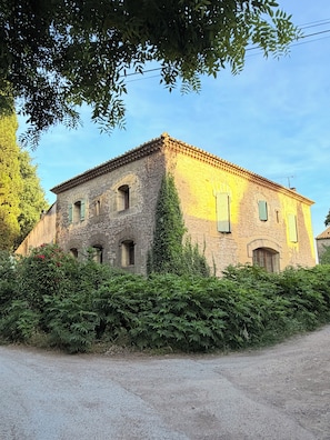 A stone building with a tiled roof, surrounded by dense greenery and a gravel path. - Authentic, spacious farmhouse in the Camargue, in a quiet location near a castle, with a private pool (Aimargues)