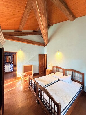 A bedroom with a wooden bed, a wooden floor, a wooden ceiling, and a door leading to a bathroom. - Authentic, spacious farmhouse in the Camargue, in a quiet location near a castle, with a private pool (Aimargues)