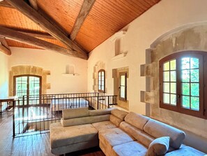 Une pièce spacieuse avec un plafond en bois, un grand canapé et un balcon doté d’une balustrade.