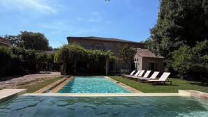 Piscina transparente com espreguiçadeiras e um edifício ao fundo.