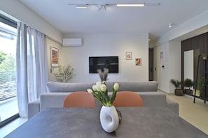 Un salon moderne avec un canapé gris, une table à manger agrémentée d’un vase blanc et un téléviseur à écran plat fixé au mur.