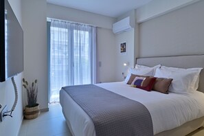 Une chambre d’hôtel avec un grand lit, un téléviseur à écran plat fixé au mur, une fenêtre avec des rideaux légers et une plante en pot.