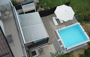 Ein Poolbereich auf dem Dach mit Schwimmbecken, Liegestühlen und Sonnenschirm.