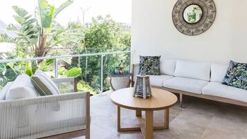 Un balcone con un divano bianco, un tavolino rotondo in legno e vista sul verde.