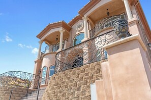 Um edifício de vários andares com fachada de pedra, grades de metal ornamentadas e janelas amplas.