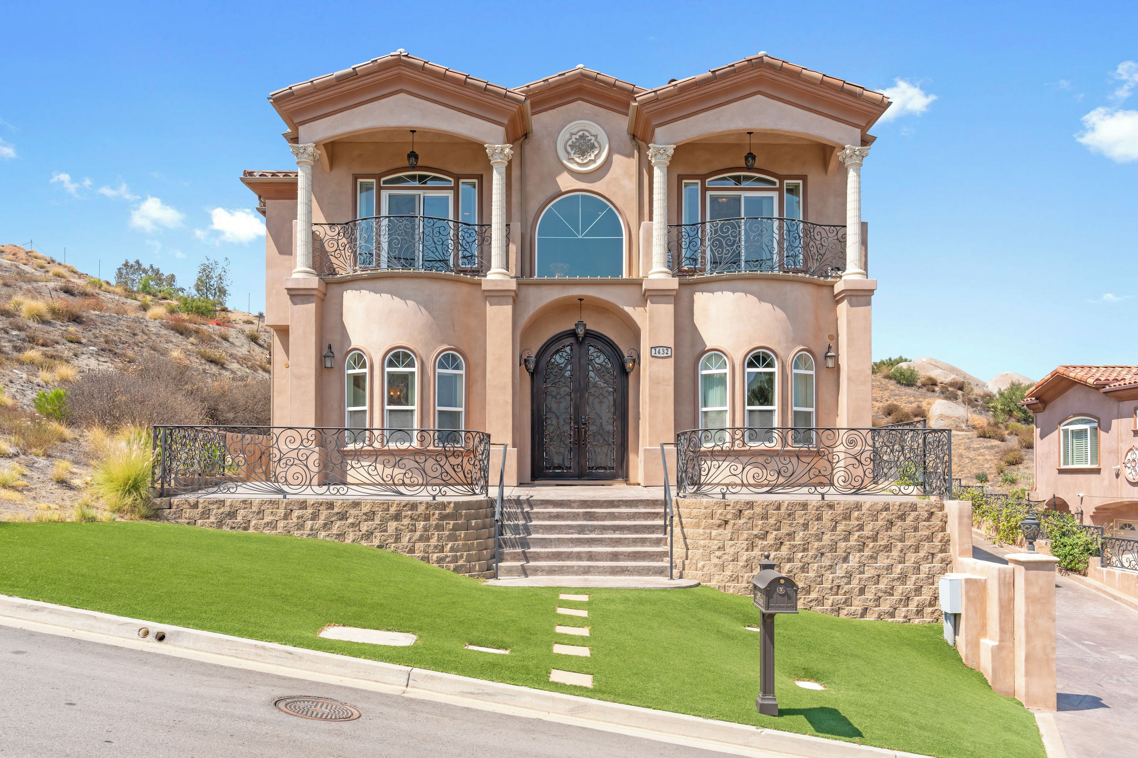 Une maison à deux étages avec une porte d’entrée noire, de nombreuses fenêtres et un escalier en pierre menant à l’entrée.