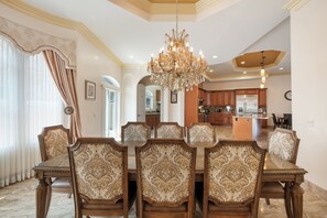 Uma sala de jantar com um candelabro, cadeiras estampadas e vista para a cozinha.