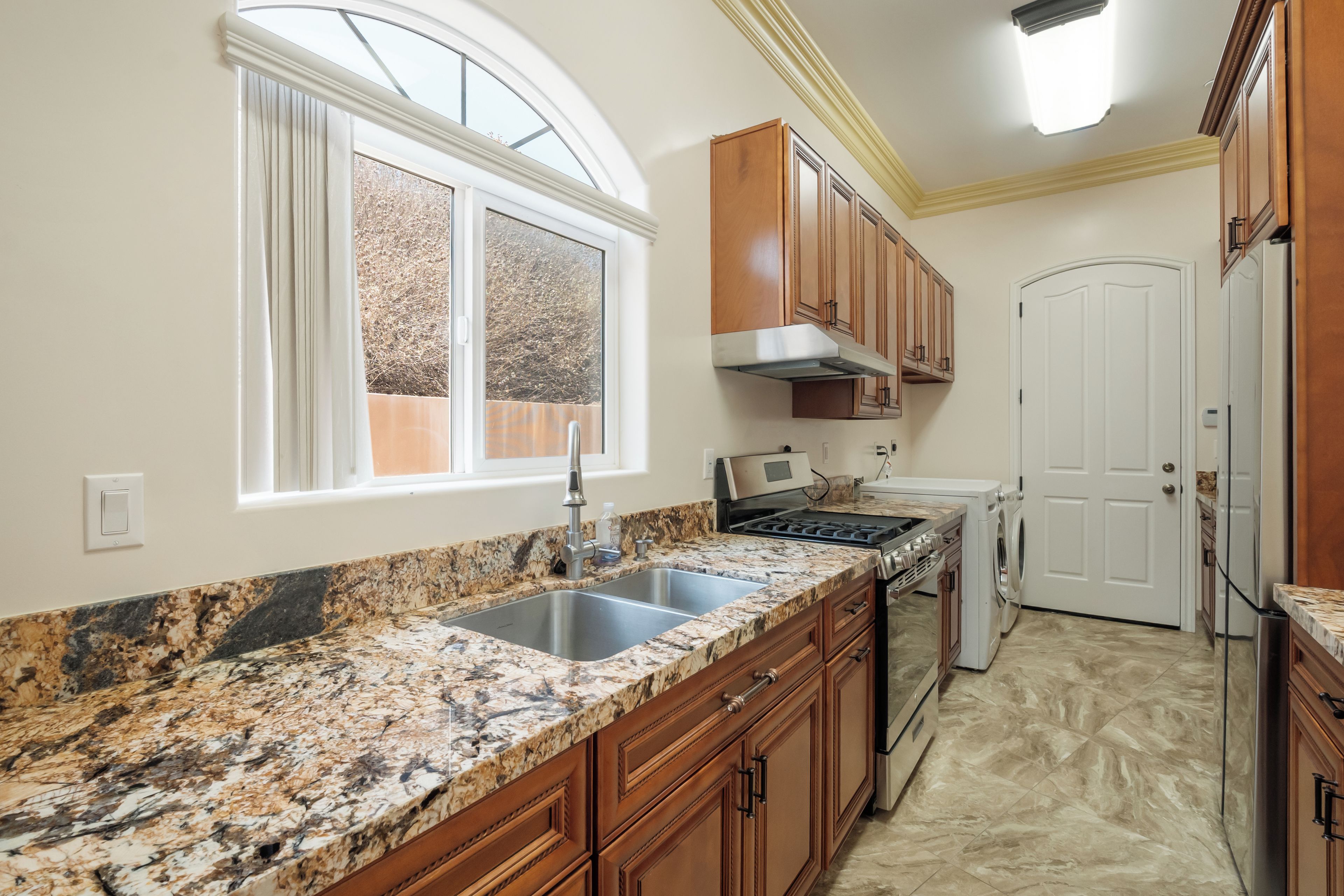 A kitchen with granite countertops, wooden cabinets, a stainless steel sink, a stove, and a built-in oven.