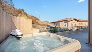 Un bain à remous avec une serviette posée sur un plateau, une clôture en bois et, au fond, un bâtiment avec un toit recouvert de tuiles.