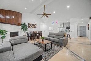 A spacious living room with a fireplace, a dining area, and a kitchen in the background. - HTX Central Retreat - Sleep 14 people - Pool table + arcade - Kingbed (Houston)