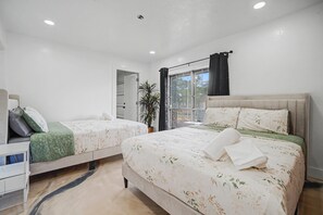A hotel room with two beds, a bedside table, a chair, a potted plant, and a window with curtains. - HTX Central Retreat - Sleep 14 people - Pool table + arcade - Kingbed (Houston)