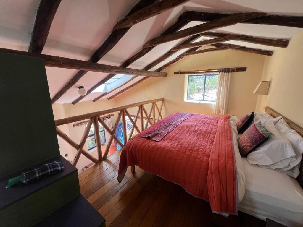 Un dormitorio con techo de madera, una cama con almohadas, una ventana con cortinas y vistas al exterior.