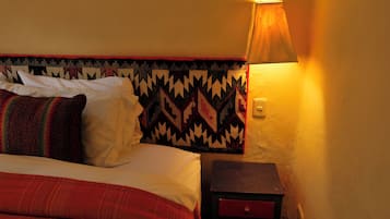 A bed with white and red bedding, a patterned headboard, and a nightstand with a lamp.