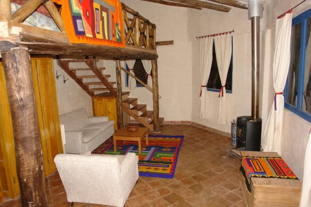 Un intérieur rustique avec un escalier en bois, un canapé blanc, une petite table et un tapis coloré.