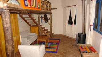 Un intérieur rustique avec un escalier en bois, un canapé blanc, une petite table et un tapis coloré.