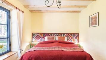 A room with a bed, a window with curtains, a patterned headboard, and a chandelier.