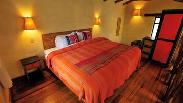 Una habitación con piso de madera, una cama con colcha naranja, dos mesitas de noche y una puerta roja.