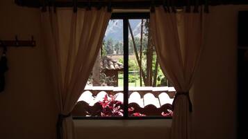Una finestra con tende, vista su un giardino e una montagna sullo sfondo.