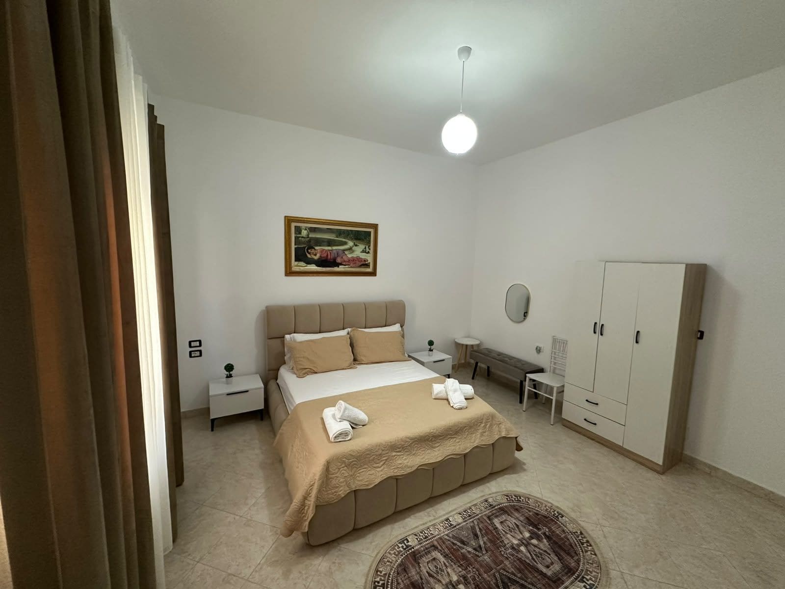 Quarto com cama, mesas de cabeceira, guarda-roupa, pintura e luminária no teto.