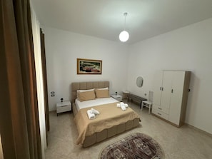 A bedroom with a bed, bedside tables, a wardrobe, a painting, and a ceiling light.
