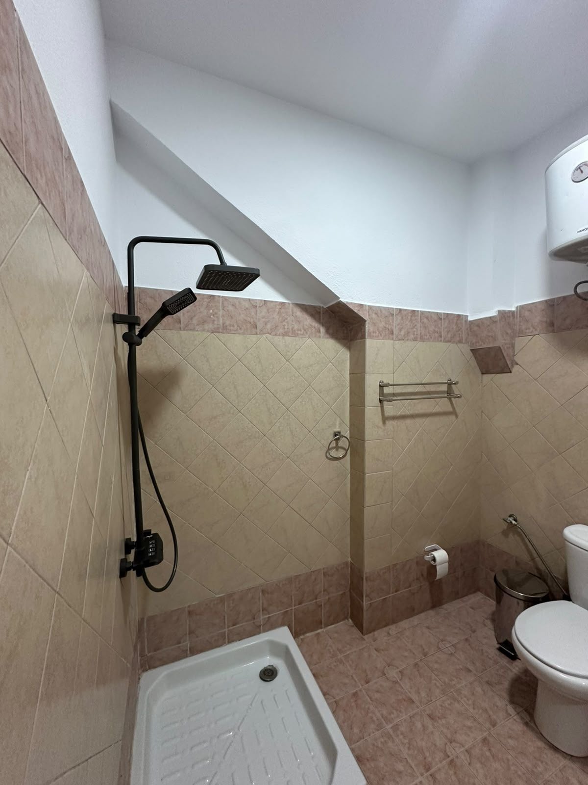 Casa de banho com chuveiro, sanita e porta-toalhas.