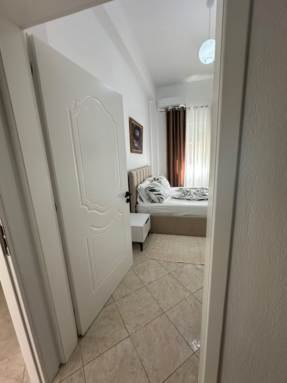 Un dormitorio con cama, mesita de noche y una puerta que da a otra habitación.