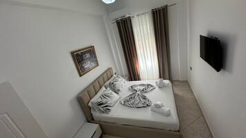 Habitación de hotel con cama, televisor de pantalla plana, un cuadro en la pared y ventana con cortinas.