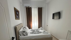 Quarto de hotel com cama, mesa de cabeceira, cadeira, televisão e cortinas.