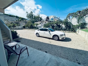 A white car parked on a gravel driveway with a building in the background. - Carcani Rooms (Gjirokastër)