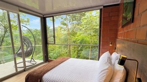 A modern bedroom with a large bed, a view of greenery through floor-to-ceiling windows, and a unique curved chair. - Samay Forest (Quito)