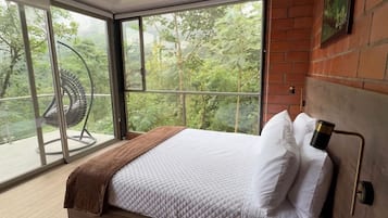 Quarto moderno com uma cama grande, vista para área verde através de amplas janelas e cabeceira de madeira.